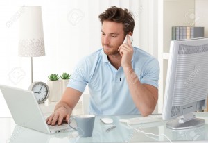 10373320-Casual-businessman-working-at-office-desk-using-mobile-phone-and-laptop-computer-typing-making-phone-Stock-Photo